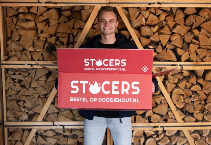 Rode doos met het logo van STOCERS wordt vastgehouden door eigenaar Cars Bijlstra. Op de achtergrond zie je gestapelde blokken eikenhout.