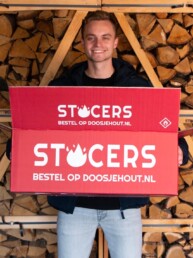 Een doos met het logo van STOCERS wordt vastgehouden. Op de achtergrond zie je gestapelde blokken eikenhout.